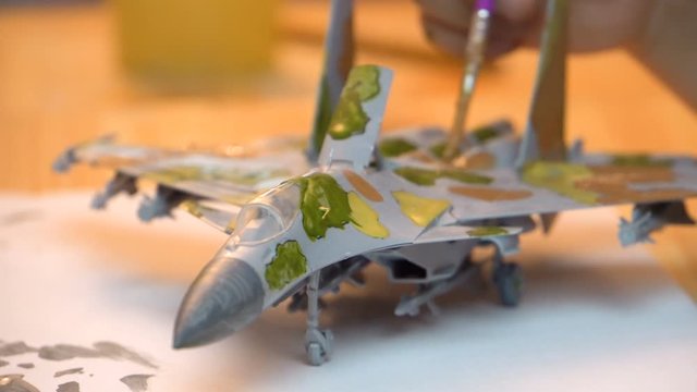 A boy paints a plane body with a brush. Military fighter. Plastic model airplane. Manual assembly of the model. Close-up.