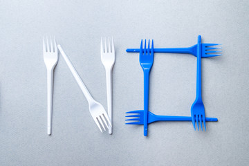 Forks made of plastic on a gray background laid out in the shape of the word no. Flat lay. The concept of protest against environmental pollution by decomposable waste.