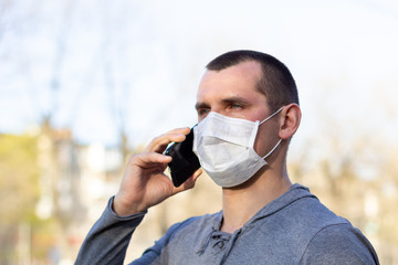 Caucasian man in medical mask on his face calling by phone. protected from virus in street outdoor.