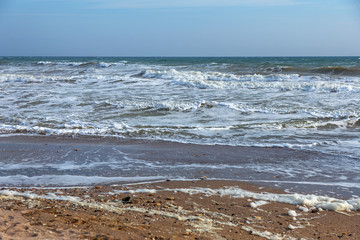 A sea wave runs onto the sand of a beach with foam on shore. Seascape in sunset colors. Beautiful natural background for design and decoration