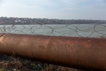 Old rusty barbed wire fence on a large rusty overpass pipe. Territory Security Wire Fence