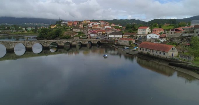 Aerial shot of the river flowing under a stone bridge and the drone ascends up and over the buildings in the town of Pontevedra, Spain