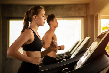 Obraz premium beautiful fit woman runner and sport man running on treadmill at fitness gym in morning light . young couple in sportswear exercise with running machine . workout people with copy space