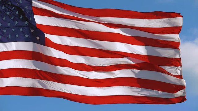 American flag is flying on a sunny day. Closeup of American flag flying in the wind against a background of bright sky. Closeup of American flag waving. USA flag flaping in wind. SUPER SLOW MOTION
