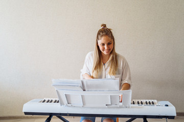 Woman is quarantined at home coronavirus. Attractive girl in a white shirt and jeans staying at home on self-isolation and playing the electronic piano - synthesizer. Hobbies - what to do at home?
