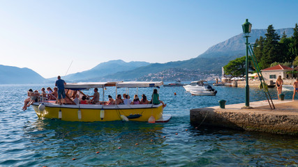 Yellow taxi boat with tourists coming out of the Rose Village - August 6, 2019 /  Lustica peninsula, Kotor Bay, Montenegro, Europe.