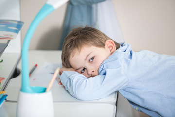 learn form home - lovely small boy in blue shirt lying on his desk