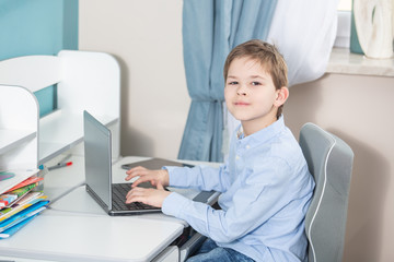 work from home - lovely boy in blue shirt sits at the desk working on his notebook computer smiling