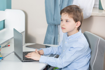 work from home - lovely boy in blue shirt sits at the desk working on his notebook computer