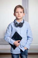 a lovely young pupil standing holding his tablet wearing headphones