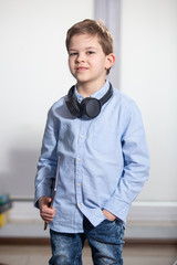 a lovely young pupil standing holding his tablet wearing headphones smiling
