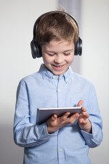 learn from home - a lovely young pupil looking at his tablet wearing headphones smiling