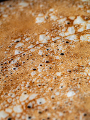 Close-up of small holes during the frying pancakes on iron frying pan. Cooking at home of delicious openwork crepes. Selective focus