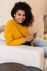 Image of cheerful african american woman using cellphone and smiling