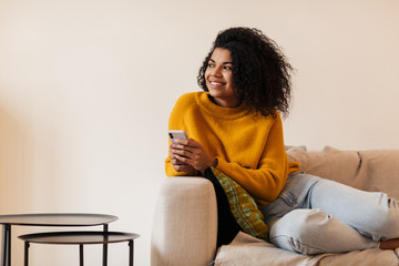 Image of smiling african american woman using cellphone while sitting