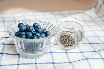 Fresh blueberry in a glass cup, and next to it in a jar are chia seeds. Concept of healthy and dieting eating.