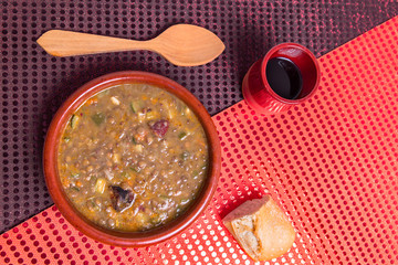 top view of lentil stew in an earthenware casserole with a piece of bread and a glass of wine