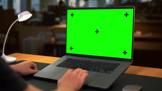 Close-up Hands of male works on Laptop computer with Mockup Green Screen with evening Office on background