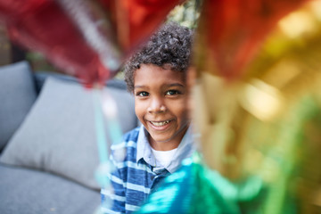 young African boy looking at camera between colorful balloons, smiling