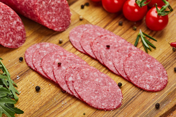 Traditional thinly sliced salami on a wooden cuttingboard  with spices, lettuce, avocado and tomatoes. Cold meat plate