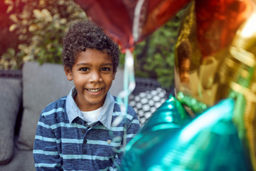 young Afro-American boy looking at camera behind colorful balloons