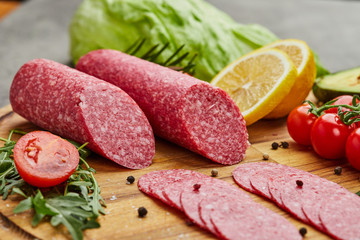 Traditional thinly sliced salami on a wooden cuttingboard  with spices, lettuce, avocado and tomatoes. Cold meat plate