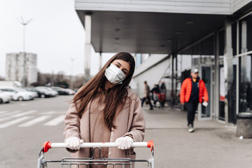 Young woman wearing protection face mask against coronavirus 2019-nCoV pushing a shopping cart.