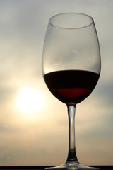 Original glass glass of red wine against a cloudy sky with a Sunny sunset and a glint of light. Concept of alcohol tasting at the festival