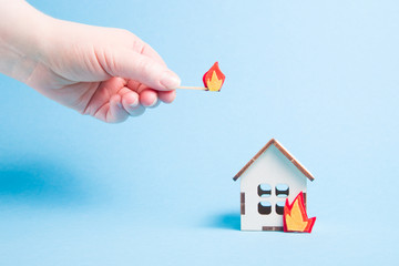 burning wooden model of a house, fire cut out of felt, blue background copy space, insurance and...