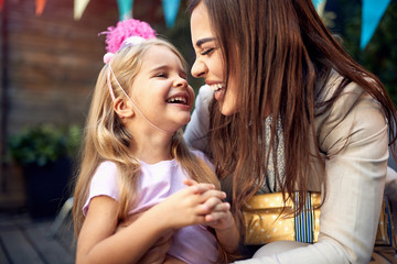 beautiful little girl giggling in a hug of a young female adult  birthday party. close relationship, love, positive emotions concept