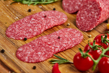 Traditional thinly sliced salami on a wooden cuttingboard  with spices, lettuce, avocado and tomatoes. Cold meat plate