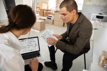 Living rooms. Female estate agent showing new home to a young man after a discussion on house plans. Choosing construction materials, repair, technologies in smart house. Moving, new home concept.