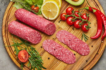 Traditional thinly sliced salami on a wooden cuttingboard  with spices, lettuce, avocado and tomatoes. Cold meat plate