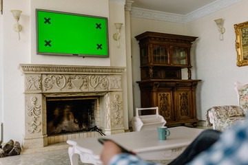 Blank green screen TV with defocused female hand holding remote control.