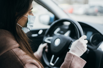 Young woman in a mask and gloves driving a car.