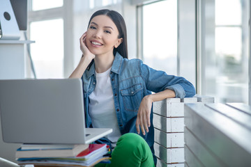 Young woman in a jeans jacket sitting on the floor and smiling nicely