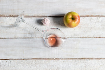 Flat lay on laying rose wine glass, sweet ball, apple, on white wooden background