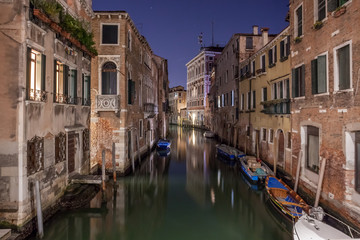 Narrow canal with boats and vintage houses at dusk. Venice city at night