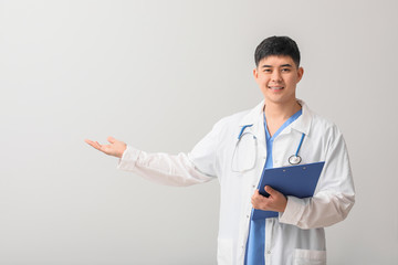 Male Asian doctor with clipboard showing something on light background