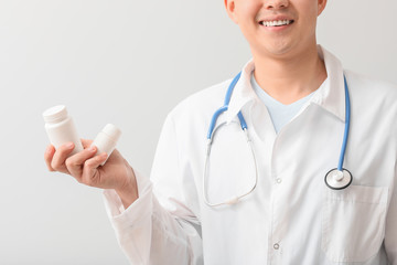 Male doctor with pills on light background