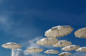 Fototapeta na wymiar ombrelloni bianchi in sequenza sparsa, su cielo blu