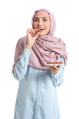 Beautiful Muslim woman eating tasty chocolate candies on white background