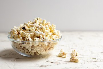 popcorn in a transparent glass bowl on white table with few popcorn beside bowl.