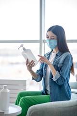 Fototapeta premium Young woman in a protective mask holding a bottle with sanitizer