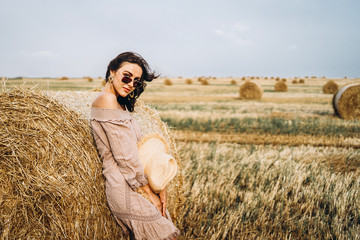 Smiling woman in sunglasses with bare shoulders on a background of wheat field and bales of hay