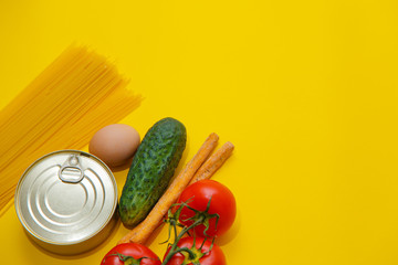 Food supplies crisis food stock for quarantine isolation period on yellow background. Pasta, canned food, cucumbers, tomatoes, egg, beans. Food delivery, coronavirus concept. 