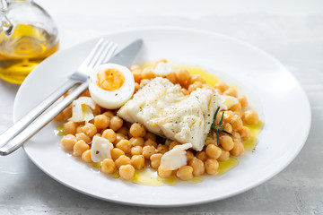 boiled cod fish with chickpea and boiled egg on white plate