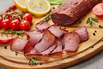 Armenian basturma or Pastirma on wooden cutting board decorated with spices, lettuce, lemon and tomatoes. Meat smoked jerky good as Beer snack