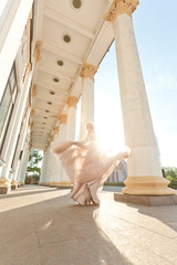 
Girl, blonde, with long curly hair, European appearance, posing near white columns in a light,...