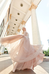 
Girl, blonde, with long curly hair, European appearance, posing near white columns in a light,...